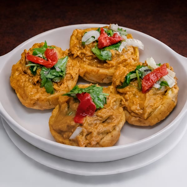 Four Cuban-style stuffed plantain cups, topped with red peppers, onions, and cilantro, in a white dish.