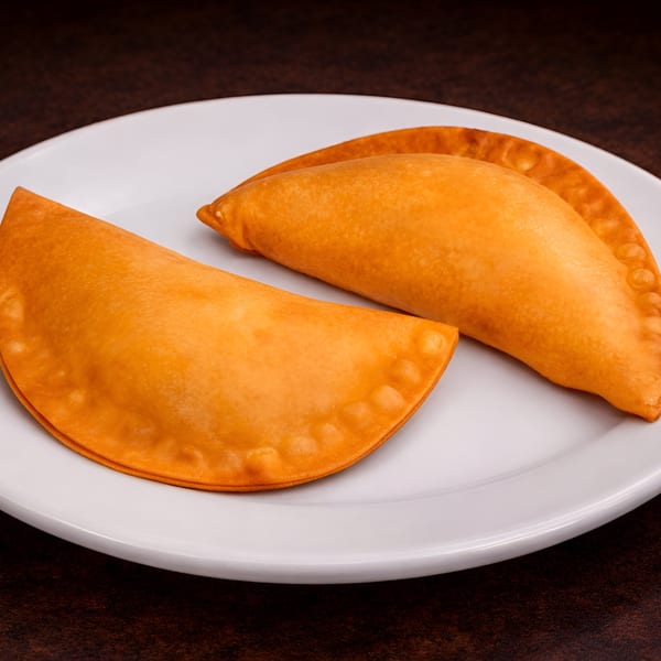 Two golden-orange Cuban empanadas with crimped edges rest on a white plate.