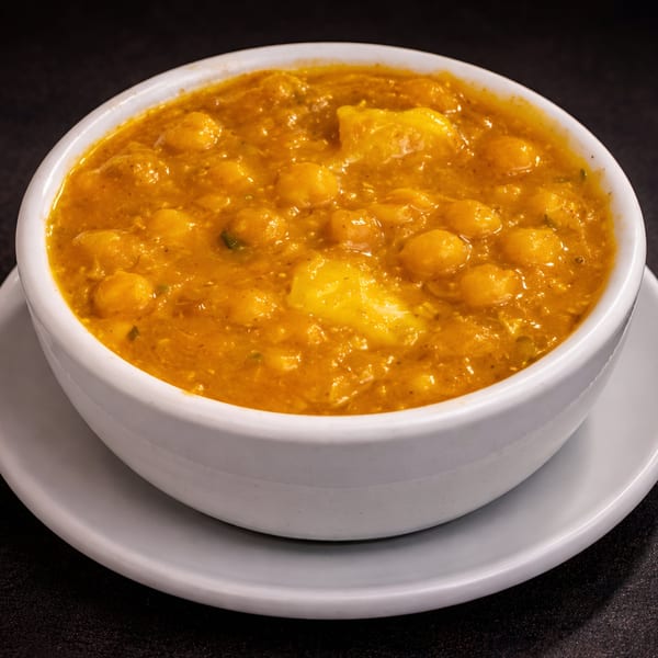 A white bowl filled with vibrant orange Cuban chickpea stew, featuring chickpeas and potato chunks.