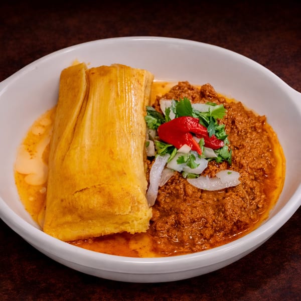 A Cuban tamal with savory ground beef, topped with onions, cilantro, and red peppers in a white bowl.