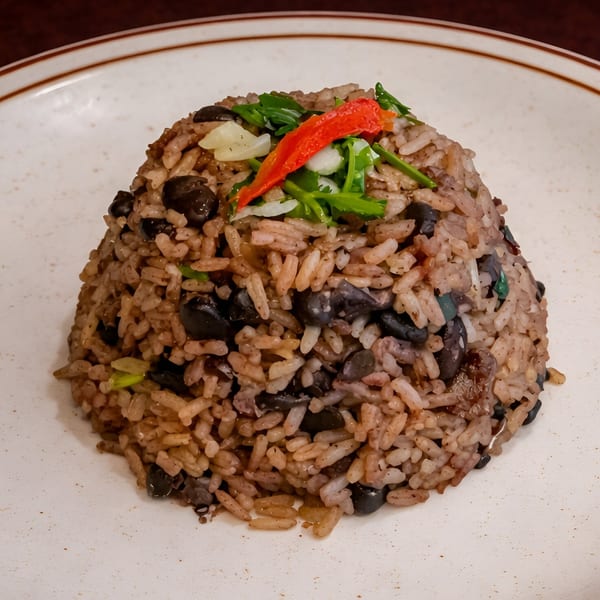 Cuban black beans and rice, topped with red pepper, cilantro, and onions on a white plate.