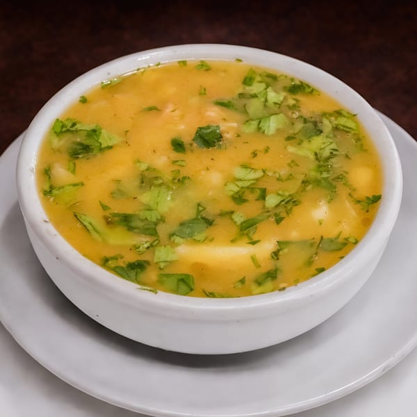 A white bowl of yellow Cuban soup, garnished with fresh green cilantro, sits on a white plate.