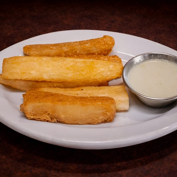 Golden fried yuca fries with a side of creamy white dipping sauce on a white plate.