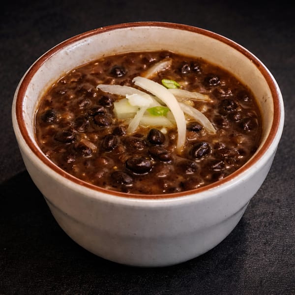 A bowl of Cuban black bean soup, garnished with sliced onions and green onions.