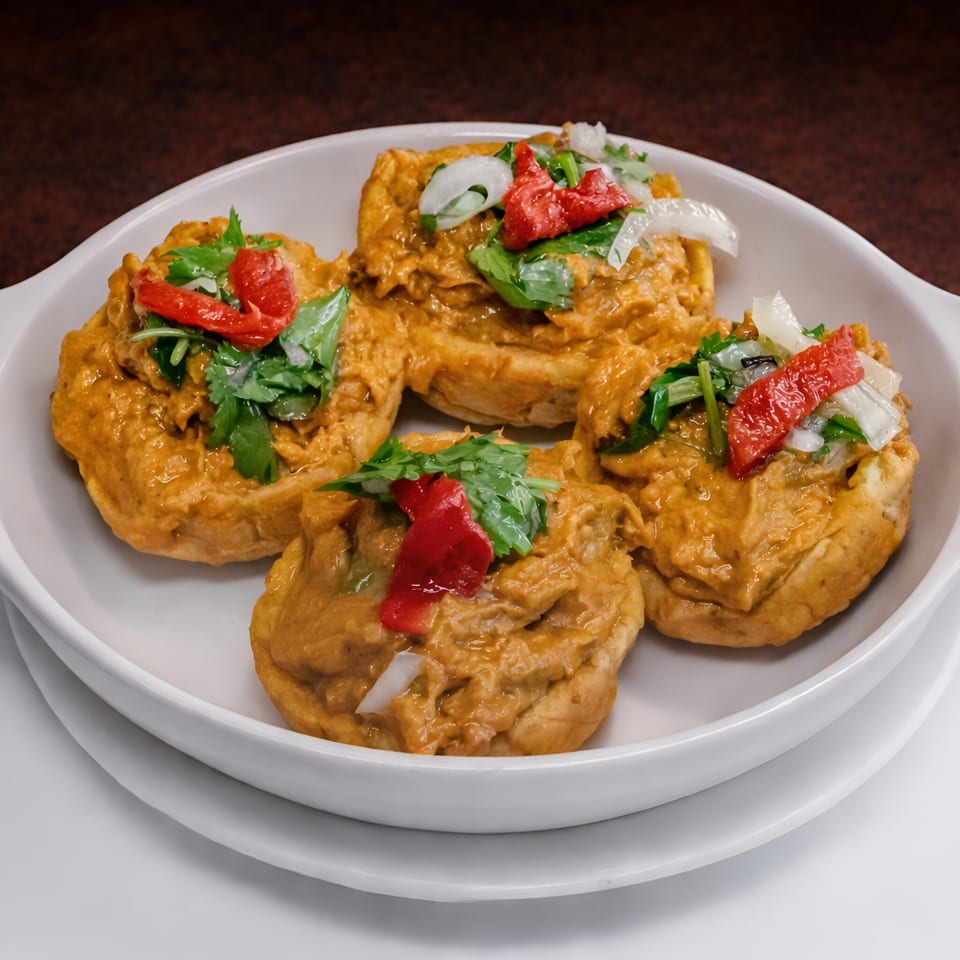 Four Cuban-style stuffed plantain cups, topped with red peppers, onions, and cilantro, in a white dish.
